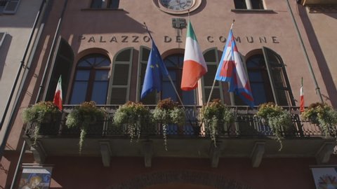 Alba, Piedmont Italy - June 23 2021:
Palazzo della comune facade (Town hall palace) in Alba, Piedmont region, Italy. European Union, Italian and Piedmont region flags, clock, bricks texture, windows.