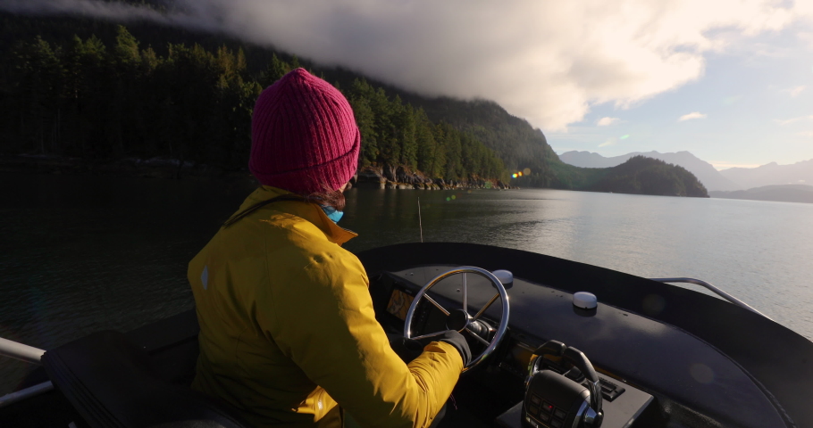 Woman Driving Motor Boat in Beautiful Nature Landscape Smiling Happy at Sunset in Coastal British Columbia Near Bute, Toba Inlet, and Campbell River. Whale Watching Tourist Travel Destination, Canada