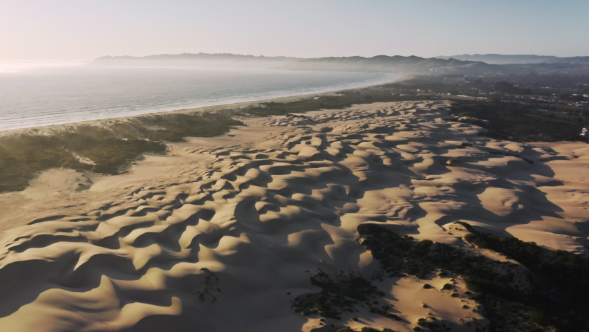 Yellow sandy slopes, washed by the beautiful calm sea as seen from above. Aerial view of sand dunes, giving protection from the ocean storms, stretching under the blue sky. High quality 4k footage