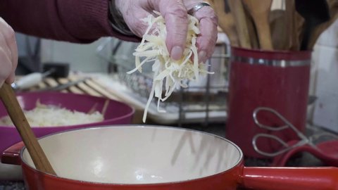 Beautiful hand puts shredded cheese on fondue pot for melting, another stirs