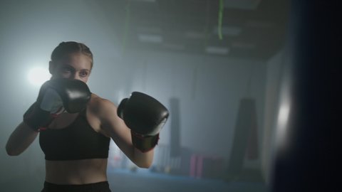 Female fighter trains his punches, beats a punching bag, training day in the boxing gym, the female strikes fast, 4k slow motion.
