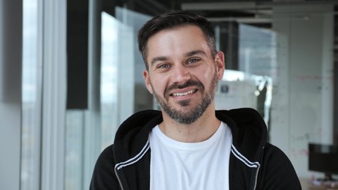 Portrait of a handsome freelance businessman in the office on a background of glass partitions. Smiling man looking at camera wearing a white t-shirt and a black sweater. Business. Successful people.
