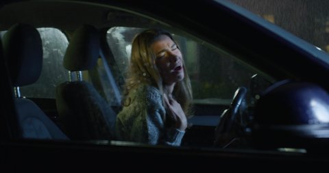 Cinematic authentic shot of young happy woman is having fun to dance and sing crazy on driver seat alone while waiting to stop raining before departure to her destination at night.