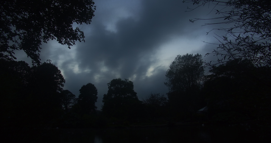Dark Gray Clouds Moving Over Trees In Silhouette On A Dramatic Sunset In Autumn. Day To Night Time Lapse. low angle