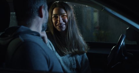 Cinematic shot of young happy woman is caressing with affection her beloved man's face in car before departure to their romantic destination together at night while raining.