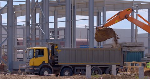 At the construction site of a plant under construction, a large, powerful, multi-axle truck is loaded the earth by an excavator