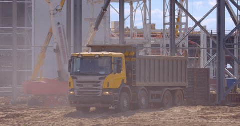 At the construction site of a plant under construction, a large, powerful, multi-axle cargo truck is driving in reverse to the place of loading 