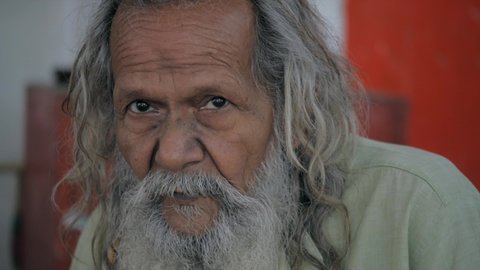 Indian old aged man with a long beard. An old person sitting outside the temple