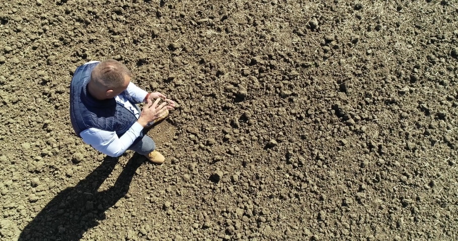 Aerial view of farmer hands checking the quality of the soil, Organic agriculture farmer assessing the ground before seeding, Drone shot of man's hands checking the soil Royalty-Free Stock Footage #1081353131
