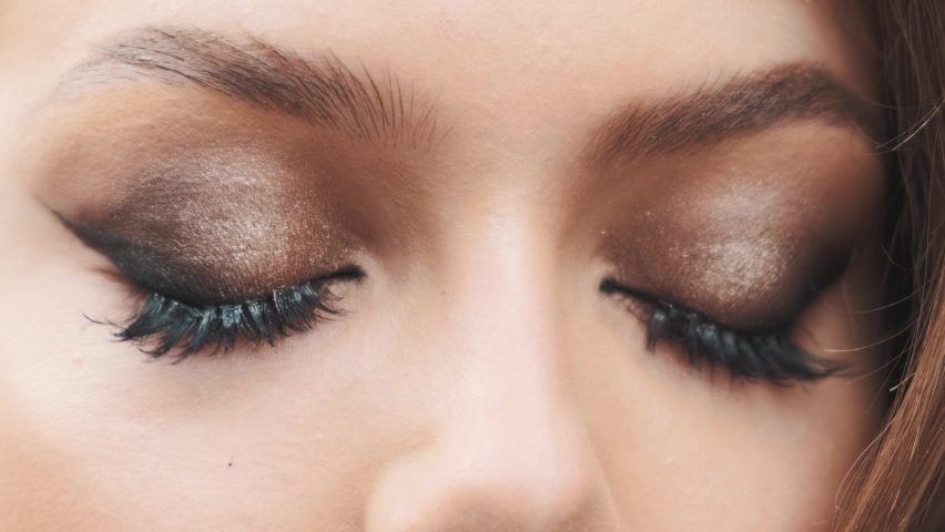 Portrait close-up of woman beautiful face. brown metallic glitter color eyeshadow fake long eyelashes. Cat eyes evening fashion makeup, sexy charming look into camera. blue gray eye open and close see
