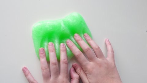 Hand Playing with textured slime with bubbles, stretching the gooey substance. Female teen hand holding green shining slime, squeezing it. Adorable Girl stretching slime toy to the sides. Liquid toy.