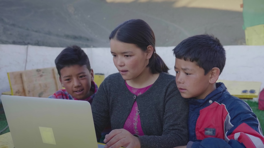 Three young East Asian rural kids sitting together outdoors and attending an online class or tuition are engrossed using a laptop in the mountainous rural village. Remote or distance education concept Royalty-Free Stock Footage #1081355357