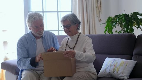 Happy mature aged older family couple unpacking carton box, satisfied with internet store purchase or unexpected gift, feeling excited of fast delivery shipping service, positive shopping experience.
