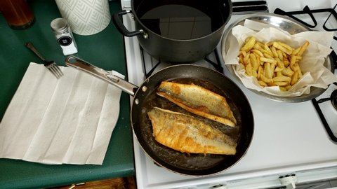 Home cooking - Top view of frying or cooking Two fillets of walleye or Yellow Pike with skin while checking with fork for readiness on non stick pan. Fish was previously battered in flour.