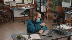 Employee looking at charts papers and laptop to work on business project and plan presentation. Man wearing face mask and working with data analysis on clipboard documents in office. - Powered by Shutterstock - Get 15% off with code: PIKWIZARD15