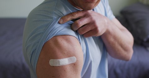 Midsection of caucasian man showing bandage on arm after covid vaccination. healthcare and lifestyle during covid 19 pandemic.