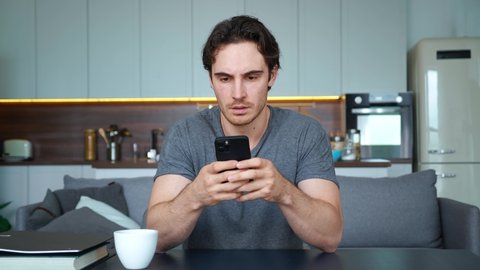 Young handsome man horrified, disappointed by what he read or seen on the screen of a mobile phone in his hands. Guy feels upset and anxious, worried about bad news. Upset and confused emotions.