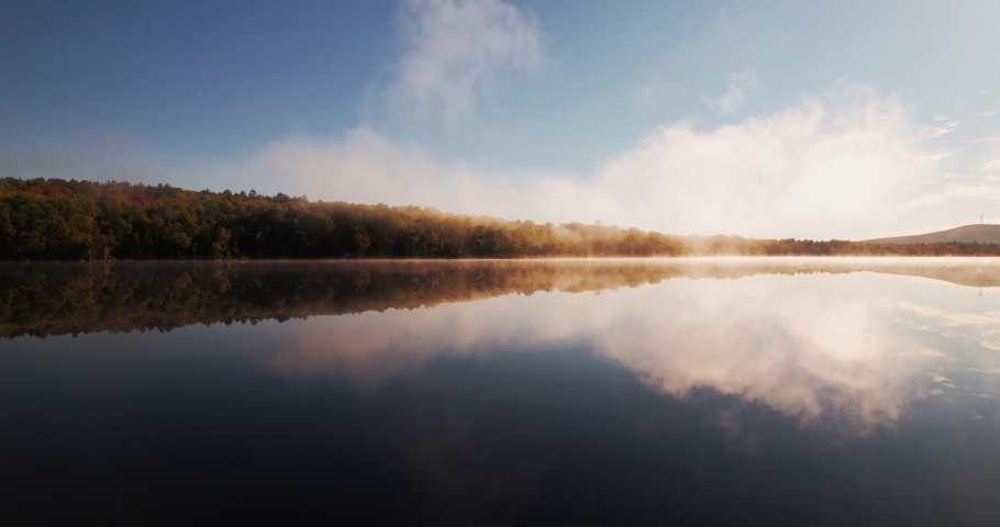 Lake Reflection During Early Morning. Foggy Sunrise Over Lake. Sunrise Over Water. Colorful Sunrise Over Lake. Foggy Morning Reflection Over Lake.