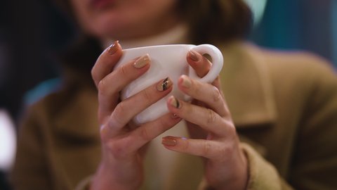 The girl holds a white ceramic cup with a hot drink and warms up in the cool evening weather. Cup in hands close up. Warming drink. Tea or coffee heated man when cold