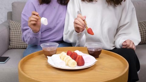two women are eating fondue, strawberries and marshmallows