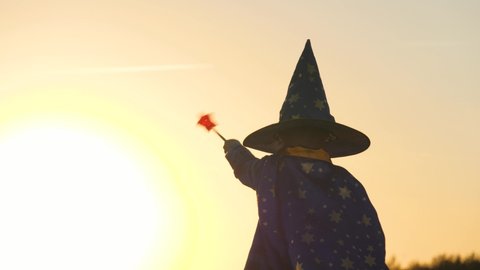 boy in a hat conjures magic wand at sunset, halluin, believe in children's magic, kid plays in the glare of the sun, child's carnival costume for holiday, an astranom festive outfit, childhood dream