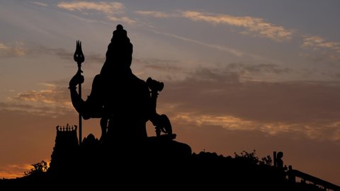 Shiva Statue Against Sky During Sunrise, Time Lapse with Bright Sun and Colorful Clodus