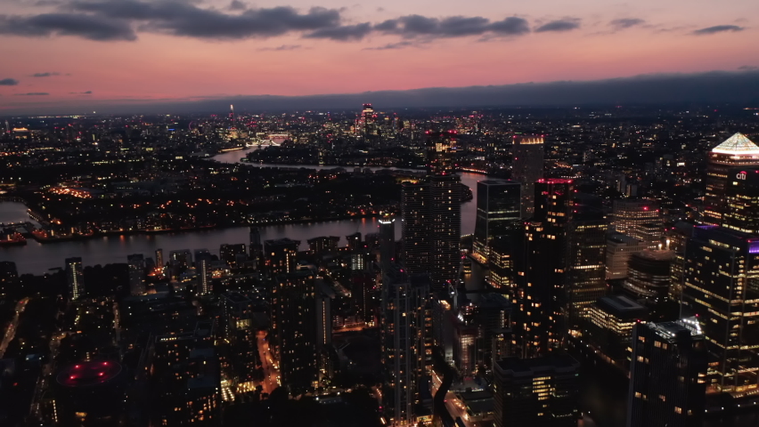 Forwards fly above night town. Illuminated streets and buildings. Cityscape against colourful sky after sunset. London, UK