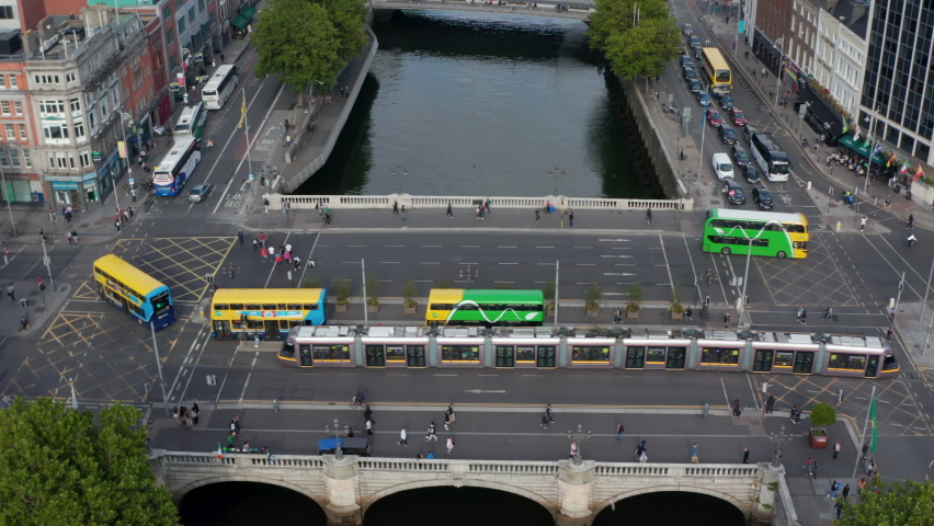 Public transport in city. Buses and tram driving on bridge across Liffey river. Tilt up reveal of cityscape. Dublin, Ireland