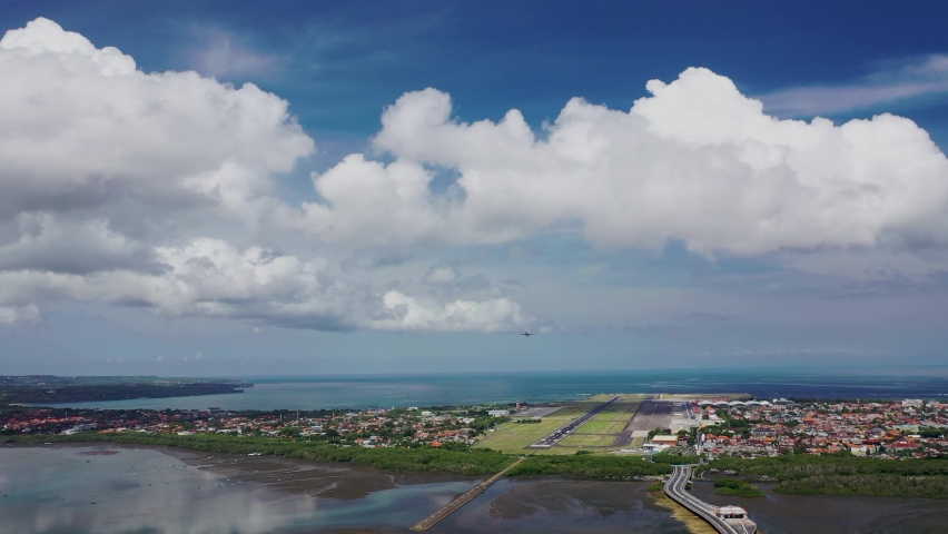 Modern large plane flies overhead. Beautiful blue sky and white fluffy clouds in the background. The aircraft takes off, landing. Day time. Aerial drone footage. International airport Bali