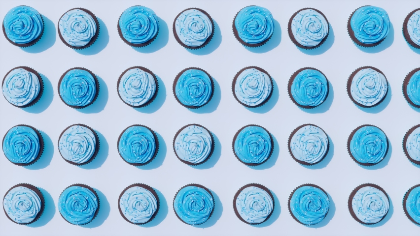 Seamless looping animation of assorted chocolate cupcakes with delicious blue cream and sweet sprinkles. Set of the homemade muffins on blue background. Decorative yummy desserts. Top view. Candy shop