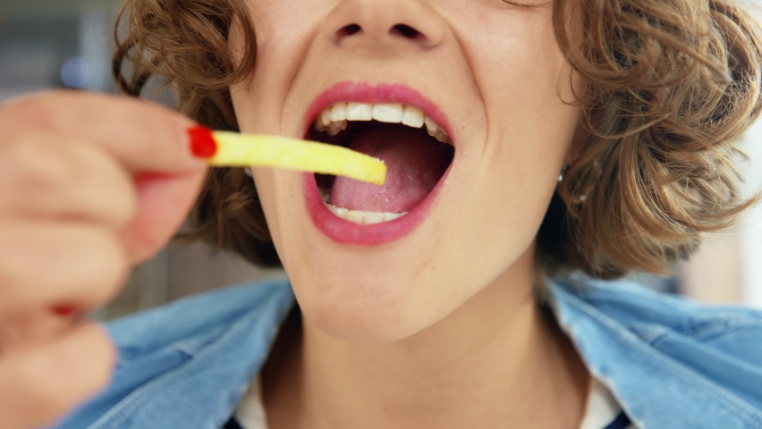 Close up on female lips and mouth eating delicious french fry. Happy and positive young woman take a bite out of potato wedge and chew on it. Tasty guilty pleasure snack at cafe or diner | Shutterstock HD Video #1081385678