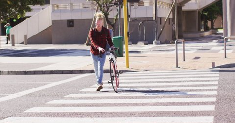 Albino african american man with dreadlocks crossing road with bike. on the go, out and about in the city.
