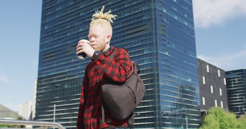 Albino african american man with dreadlocks walking and drinking coffee. on the go, out and about in the city.