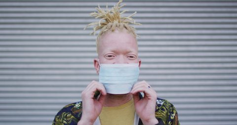 Portrait of albino african american man with dreadlocks wearing face mask. on the go, out and about in the city during covid 19 pandemic.