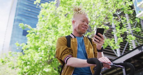 Happy albino african american man with dreadlocks in park with bike talking on smartphone. digital nomad on the go, out and about in the city.