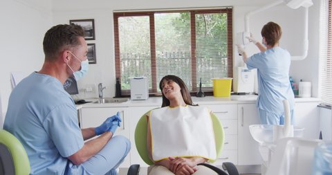 Caucasian male dentist with face mask preparing smiling female patient at modern dental clinic. healthcare and dentistry business during covid 19 pandemic.