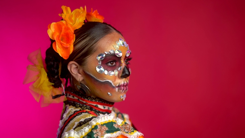 Girl with beautiful eyes blinks and looks straight to the camera. Girl in folklore costume and day of the dead style make up. Mexico culture, fashion and traditions. Day of the dead 2021. Royalty-Free Stock Footage #1081396898