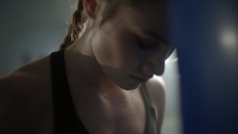 Woman power, tired female fighter stands pressed against a punching bag, hard training in the boxing gym, 4k slow motion.
