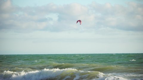 Kitesurfing on the waves of the emerald sea. The man is kiteboarding in the turquoise sea water. The man on the board quickly floats through the waves. Summer vacation.