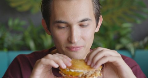 Close up shot of handsome men are eating burger in fast food restaurant. People eat unhealthy meal. Getting satisfaction from unhealthy food. Junk food, modern life concet. Front view, slow motion