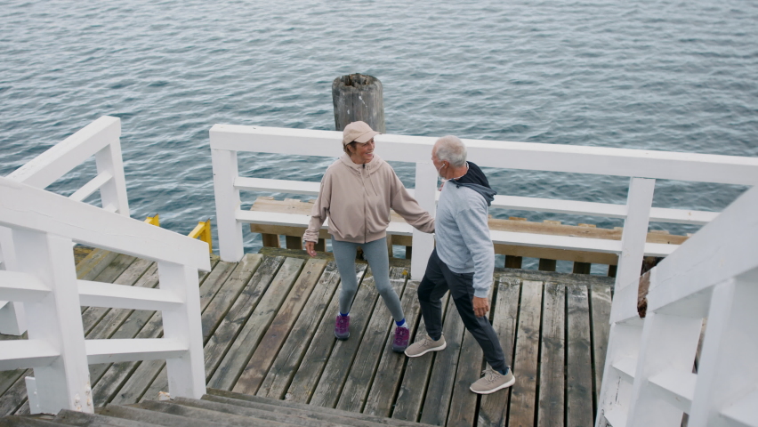 Senior couple outdoors on pier by sea at the morning, hugging after run.