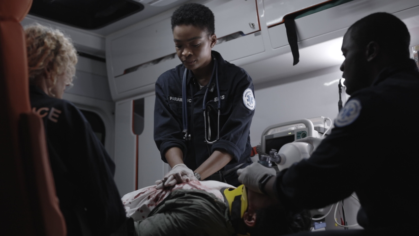 Multi ethnic emergency care assistants rescuing unconscious man with defibrillator while riding in ambulance car to hospital. First aid concept. Royalty-Free Stock Footage #1081403384