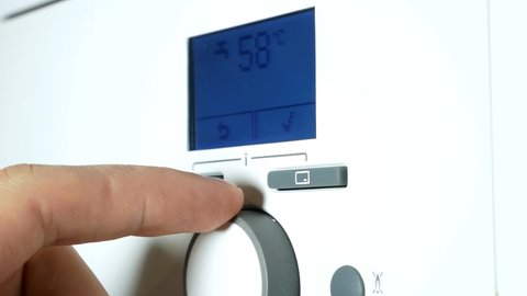 Fingers adjust Gas boiler control panel for hot water and heating. Buttons and a digital display. Сoncept of home heating and heat conservation.