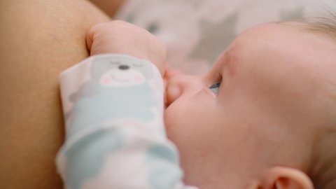 Infant sucks the mother's breast, close-up. Baby is resting and relaxing, enjoying sucking the mother's breast. Natural feeding of the child. Healthy food for a child. Motherhood and child care.