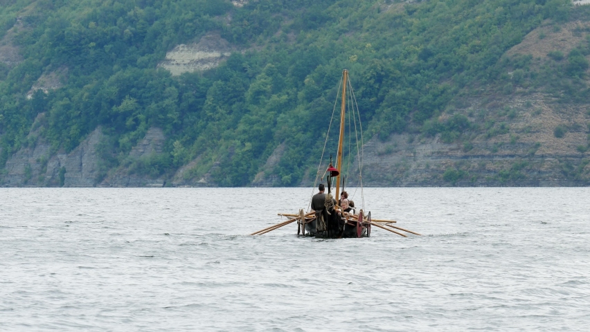 Vikings Sail on an Old Ship with a Lowered Sail on a Quiet River in the Fog. Concept on the theme of the Vikings and the early Middle Ages.