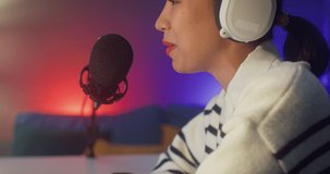 Happy asia lady blogger music influencer record a podcast on computer with headphones and microphone talk with audience in living room home studio at night. Stay at house, Content creator concept.