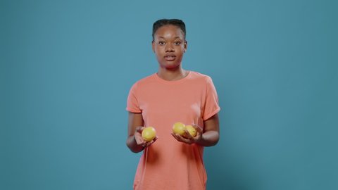 Positive woman juggling with fresh lemons and smiling in front of camera. Young adult trying to juggle with yellow citrus fruits, advertising organic and natural vitamins. Funny vegetarian