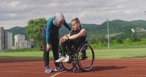 group of multi cultural sports people disabled female and her trainer wearing hijab after training on athletics sports track checking data on a smartwatch.