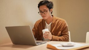 slow motion scene young asian man drink hot coffee during using laptop to checking mail , manage task and contact with team at living room in house for work from home lifestyle concept