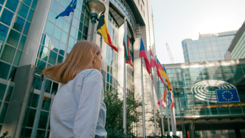 Back view of Woman Walking along EU Flags to European Parliament Office in Brussels, Belgium. Politics, Economy and Business Concept. 4K gimbal follow low angle shot in slow motion Royalty-Free Stock Footage #1081427498